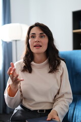 Hispanic young adult female engaged in conversation on blue sofa in bright room