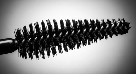 Obraz premium Close up of a black mascara brush with a spiral bristle arrangement, set against a gradient gray background for beauty concepts.