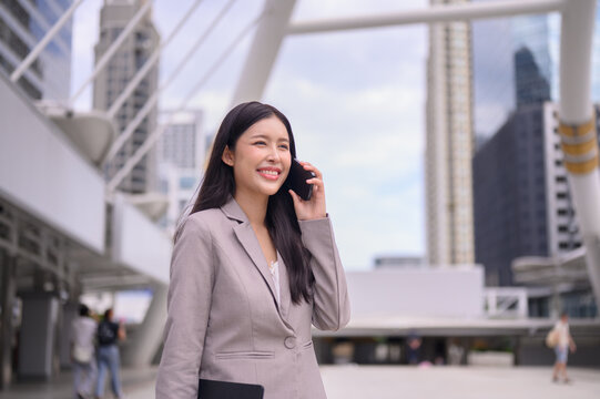 Asian female executive talking on  phone outdoors, surrounded by skyscrapers.