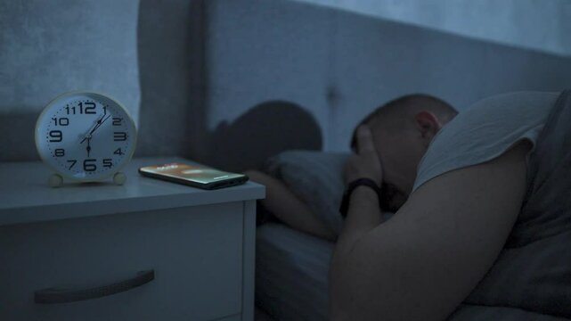 Young man trying to turn off a ringing alarm clock at morning. Close-up of hand reaching out to stop the alarm clock, to waking up at six o'clock