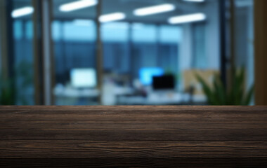 Wooden tabletop in modern office setting with blurred background featuring workstations and plants
