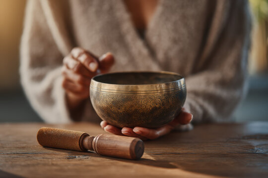 A person gently holds a singing bowl in one hand while sitting in a peaceful indoor setting, engaged in a meditation practice that promotes tranquility and mindfulness