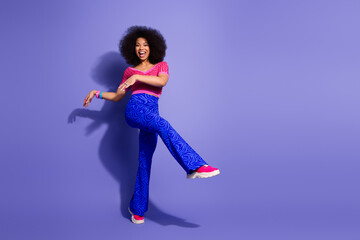 Young woman dancing joyfully in retro-inspired outfit and vibrant colors against a purple background, showcasing positive energy