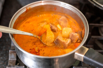 Making massaman curry. Stirring the dish with a spoon in a saucepan on the stove