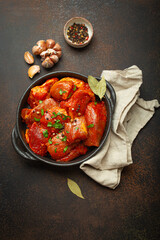 Raw uncooked chopped pieces of meat marinated with seasonings and parsley in black casserole dish top view on dark rustic background. Cooking ragout stew with marinated meat fillet pieces.