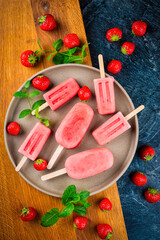 Frozen dessert- homemade strawberry ice lolly popsicle  with yogurt and fresh strawberries offered as top view on a design plate