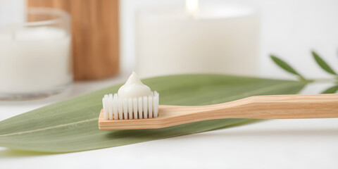 A bamboo toothbrush holds a dollop of white organic toothpaste beside a soft green leaf