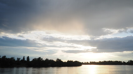 Witness the breathtaking spectacle of clouds as they dance across the sky, casting shadows over calm waters at sunset. Natures palette transitions with stunning hues of orange and blue