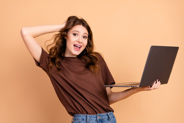 Young woman holding a laptop in a happy mood, showing casual style with brown hair and beige...