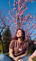 Young woman enjoying springtime under pink cherry blossom tree in sunny park