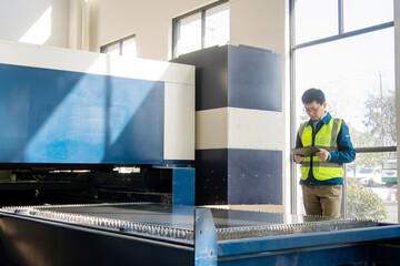 Asian engineers operating laser cutting machine with digital tablet