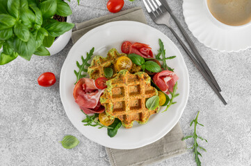 Spinach waffles with tomatoes, arugula and prosciutto on a white plate with a cup of coffee. Healthy breakfast. Top view