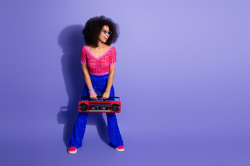 Trendy young woman with afro holding a vintage boombox against a vibrant purple background