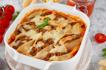 Baked stuffed pasta conchiglioni shells with meat, tomato sauce, cheese and basil in a white ceramic form. Italian cuisine.