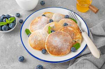 Delicious homemade pancakes with blueberries and honey, sprinkled with powdered sugar on top on a gray concrete background.