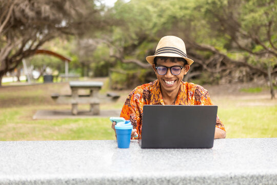 Indonesian man in Australia wearing batik, using laptop outdoors