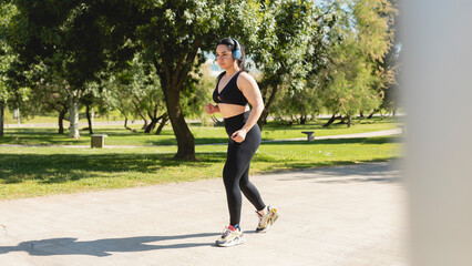 A concentrated young woman listens to music with headphones before starting a run in the park.
