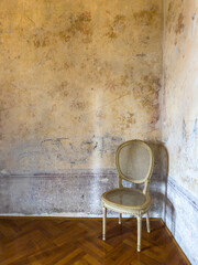 vintage corner with a wicker chair against a textured, aged wall and herringbone wooden floor. raw,...