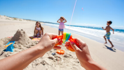  POV hands prepare colorful kite for family beach day fun as children play in summer sun. Active outdoor vacation, creating joyful childhood memories concept