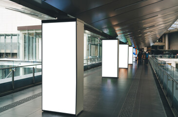 Modern indoor walkway with row of vertical blank billboards ready for advertising, creating clean futuristic feel in high-traffic public area with glass railings and lights