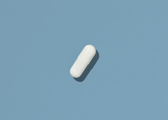 White Medical capsule on blue top view, hard shadows. Taking dietary supplements
