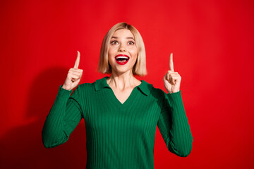 Excited young woman in a green sweater gesturing upward against a vibrant red background