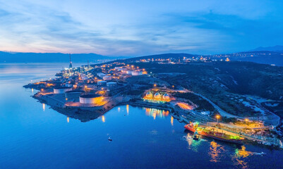 Aerial view of INA Oil Refinery with storage tanks and harbor illuminated at night, Rijeka, Croatia.