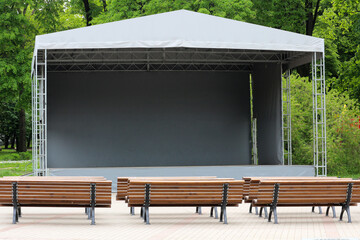 Portable mobile stage with tent cover and aluminum frame with Wooden Benches in Park Setting