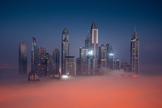 Aerial view of modern skyscrapers illuminated by city lights under a cloudy night sky, Dubai Marina, Dubai, United Arab Emirates.