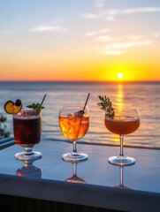 Three cocktails on a table at sunset overlooking the ocean in a tropical location with bright orange sky and sun