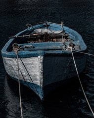 An old but sturdy wooden fishing boat floating in deep, dark waters. The hull of the boat is...