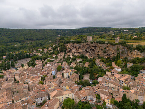 Aerial view of picturesque medieval village with stone houses and charming rooftops on a cliff surrounded by greenery, Cotignac, Var, France.