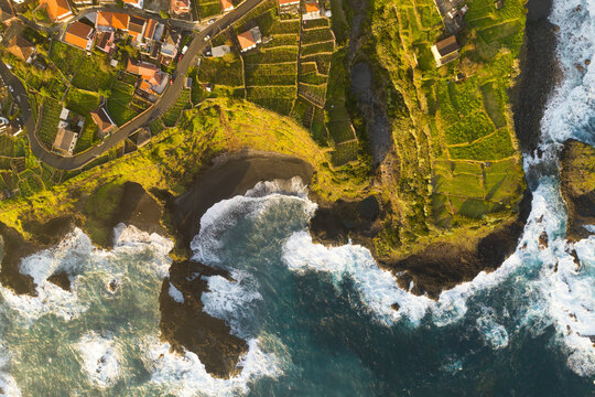 Aerial view of beautiful coastline with vibrant village and lush fields, Madera, Portugal.