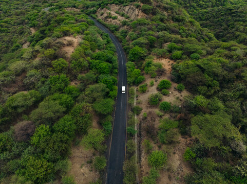 Aerial view of a winding road with a white van traveling through lush forests and rugged mountains, Southern Nations Nationalities and Peoples' Region, Ethiopia.