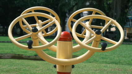 Outdoor fitness equipment with four yellow rotating wheels in a park setting. Ideal for themes of...