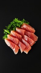 Close-up of fresh tuna sashimi slices arranged on a black plate with lettuce garnish studio shot from above