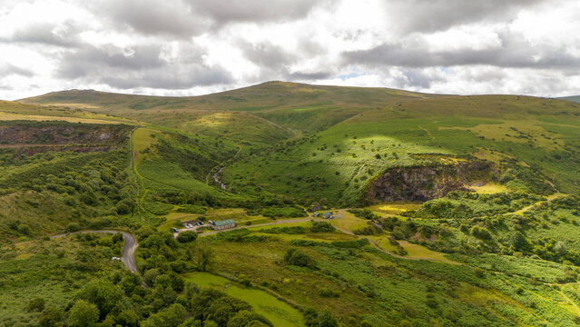 Aerial view of lush rolling hills and a serene valley with a winding road under a cloudy sky, Meldon, Okehampton, England.