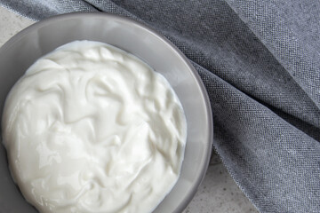 Gray bowl with white natural yogurt on the stone marble table.