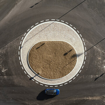 Aerial view of a blue car driving along a roundabout in Osnago, Lombardy, Italy.