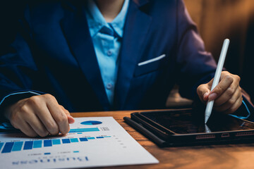 Business professional analyzing data reports on tablet while holding stylus and reviewing...
