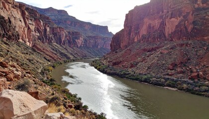 Deep river flows through tall, layered canyon walls under a partly cloudy sky