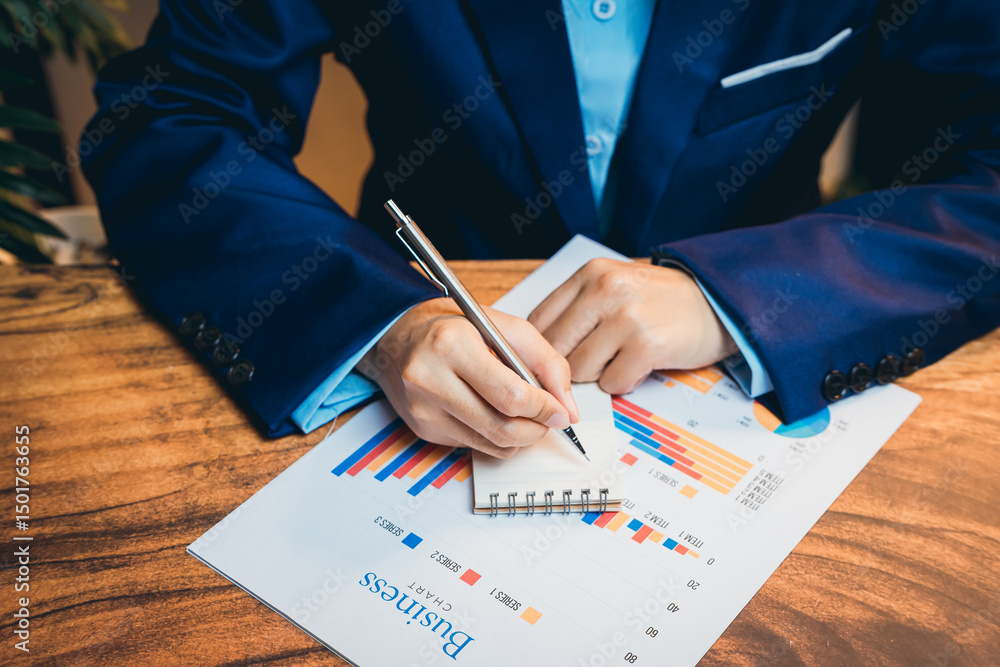 Poster business professional writing analysis on notepad while reviewing colorful graphs and charts on tabl