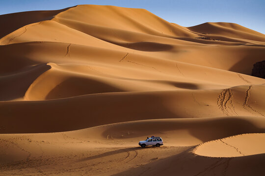 Aerial View of an off road vehicle driving among the sand dunes at sunset in the Sahara desert, Djanet, Algeria, Africa.