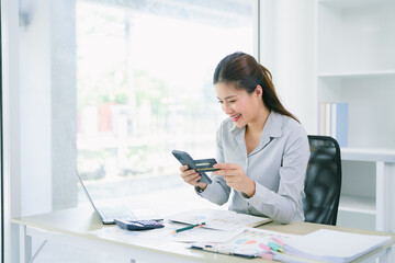 Beautiful Asian woman using smartphone buying online shopping by credit card while wear sweater sitting on desk in living room at home. Lifestyle woman at home concept.