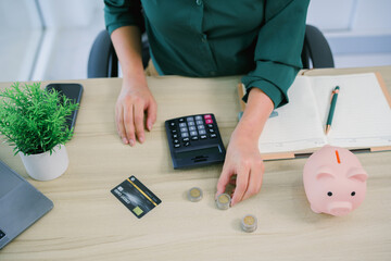 Saving money wealth concept, asian young business woman hand putting coin into piggy for saving cost, cash finance planning to spend enough money on her income for save money, payment tax, investing.
