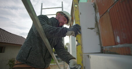 Aligning insulation panel with spirit level, construction worker on scaffold ensuring accurate...