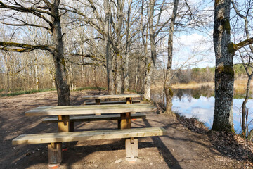 
Two wooden picnic tables with benches located by a reservoir with trees and blue sky reflection in the water.