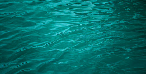 Obraz premium Reflection of light on the wavy surface of the blue-green water background. Ripples. Beautiful teal background with copy space for design. Web banner. Wide. Panoramic