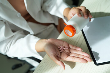 An asian young doctor is holding an medicine bottle to assess the quality of medicine and recommending medication and treatment to patient and explaining the dose and description of the medication.