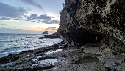 Cave entrance on rocky beach, ocean sunset, horizon view through opening